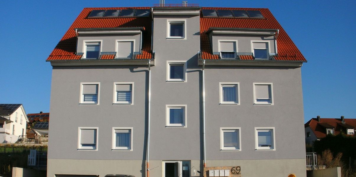 Ein saniertes Mehrfamilienhaus mit grauer Fassade und rotem Dach